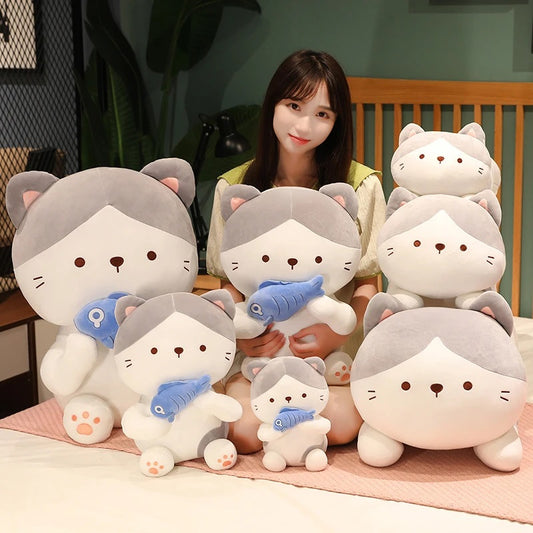 woman sitting beside multiple sizes of kawaii cat holding a fish plush