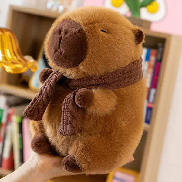 A 35cm brown capybara plush with a knitted scarf being held by a person, displayed against a colorful bookshelf background.