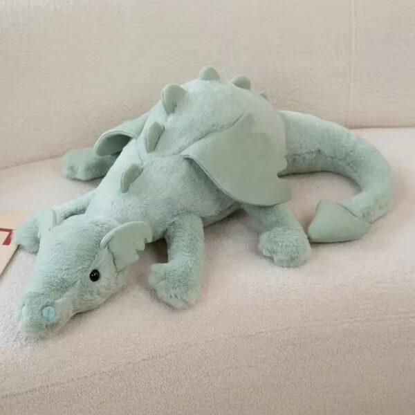 A soft and cuddly green dragon plush toy with plush wings and spikes, resting on a cozy couch.