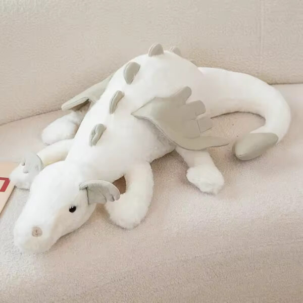 A soft and fluffy white dragon plush toy with light gray wings and spikes, resting on a cozy couch.